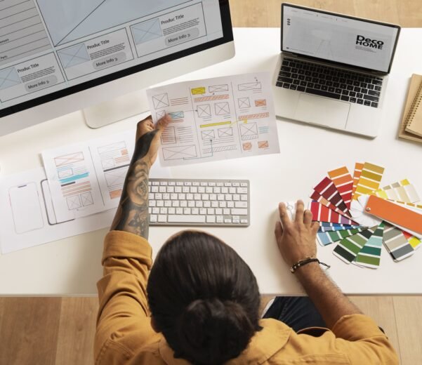 مصمم يعمل على بروفايل شركة مضاهاً مخططات واجهات ومخططات Wireframes مع لوحة ألوان وكوب قهوة على مكتب أنيق